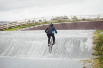 Visão traseira do ciclista andar de bicicleta BMX no parque de skate — Fotografia de Stock
