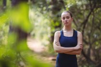 Portrait of beautiful woman standing with arms crossed in forest — Stock Photo