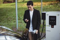 Людина використовує мобільний телефон під час заряджання автомобіля на зарядній станції електромобіля — стокове фото
