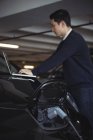 Man using laptop while charging electric car in garage — Stock Photo