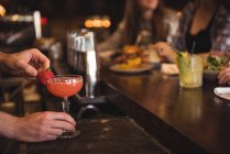 Крупный план бармена, держащего коктейль у барной стойки — стоковое фото