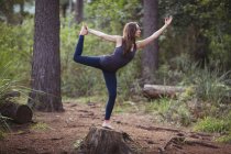 Жінка, що виконує стоячий лук позує йогу в лісі на сонячний день — стокове фото