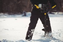 Mid section of ice fisherman drilling in snow — Stock Photo