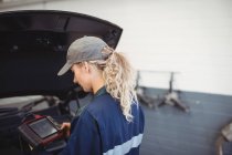 Mecânico feminino usando dispositivo de diagnóstico eletrônico na garagem — Fotografia de Stock