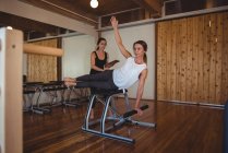 Entraîneur aidant femme tout en pratiquant pilates dans le studio de fitness — Photo de stock