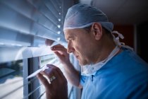 Хірург, який дивиться через віконні жалюзі в лікарні — стокове фото