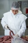 Female butcher cutting sausages with knife at meat factory — Stock Photo