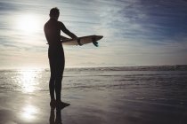 Silhouette of surfer standing with surfboard on beach — Stock Photo