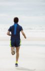 Вид сзади спортсмена, бегущего по мокрому пляжу — стоковое фото