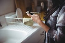Sección media de la mujer usando el teléfono móvil en la cocina - foto de stock