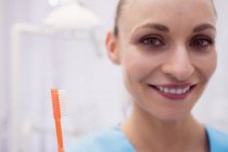 Retrato de dentista feminina segurando escova de dentes na clínica odontológica — Fotografia de Stock