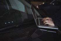 Las manos del hombre usando el ordenador portátil en el coche en el garaje - foto de stock