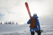 Vista trasera del esquiador caminando con esquí en la montaña cubierta de nieve - foto de stock
