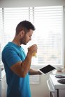Man using his digital tablet while having glass of juice in kitchen at home — Stock Photo