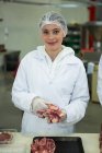 Retrato de la carnicera sonriendo mientras sostiene la carne en la fábrica de carne - foto de stock