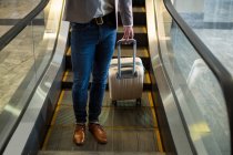 Low section of businessman standing on escalator with luggage at airport — Stock Photo