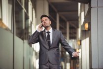 Empresario hablando por teléfono móvil mientras camina por el pasillo de la oficina - foto de stock