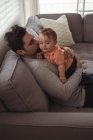 Padre besando a su bebé en el sofá en la sala de estar en casa - foto de stock