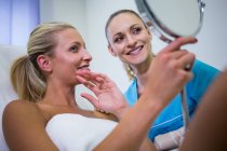Happy patient checking skin in mirror after receiving cosmetic treatment — Stock Photo