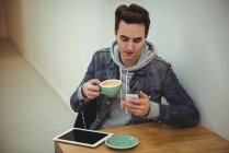Чоловік використовує мобільний телефон, тримаючи чашку кави в кав'ярні — стокове фото