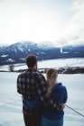 Couple avec les bras autour debout sur un champ enneigé contre le ciel — Photo de stock
