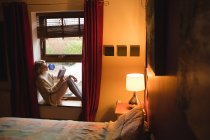 Frau sitzt am Fenster und liest zu Hause ein Buch — Stockfoto