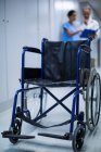 Пустое инвалидное кресло в коридоре больницы с врачами, говорящими на заднем плане — стоковое фото