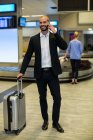 Бізнесмен з багажем розмовляє на мобільному телефоні в зоні очікування в терміналі аеропорту — стокове фото