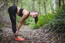 Улыбающаяся женщина, выполняющая упражнения на растяжку в лесу — стоковое фото