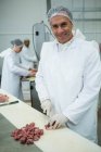 Retrato de açougueiro cortando carne em pequenos pedaços na fábrica de carne — Fotografia de Stock