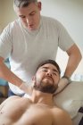 Physiothérapeute examinant le cou d'un patient de sexe masculin en clinique — Photo de stock