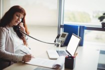 Беременная деловая женщина разговаривает по телефону во время работы в офисе — стоковое фото