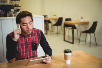 Мужчина разговаривает по мобильному телефону во время использования цифрового планшета в кафе — стоковое фото