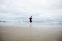 Hombre en traje de baño y gorra de natación corriendo en la playa - foto de stock
