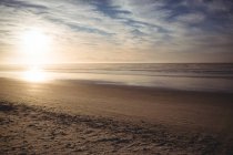 Vue tranquille sur la plage avec ciel nuageux et soleil éclatant — Photo de stock