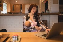 Madre che allatta il bambino mentre usa il computer portatile a casa — Foto stock