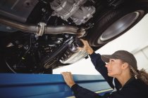 Feminino mecânico examinando um carro com lanterna na garagem de reparação — Fotografia de Stock