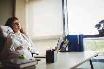 Grávida empresária segurando dor nas costas enquanto sentado na cadeira no escritório — Fotografia de Stock
