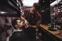 Homem recebendo barba aparada por cabeleireiro com tesoura na barbearia — Fotografia de Stock