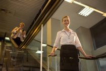 Retrato del personal femenino bajando de la escalera mecánica en la terminal del aeropuerto - foto de stock