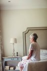 Продумана старша жінка сидить на ліжку в спальні — стокове фото