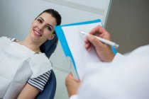 Доктор написання буфер обміну лежачи пацієнта на стоматологічний ліжко в стоматологічній клініці — стокове фото