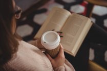 Жінка читає книгу, маючи каву у вітальні вдома — стокове фото