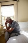 Беспокойный старший мужчина сидит на кровати в спальне дома — стоковое фото