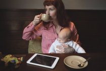 Mère prenant un café tout en tenant bébé dans un café — Photo de stock