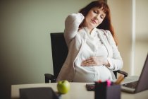 Femme d'affaires enceinte tenant mal au dos alors qu'elle était assise sur une chaise au bureau — Photo de stock