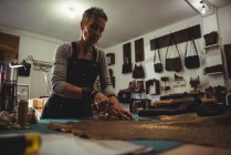 Aufmerksame Handwerkerin schneidet Leder in Werkstatt — Stockfoto