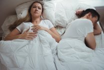 Стурбована жінка лежить, поки чоловік спить поруч з нею в спальні вдома — стокове фото