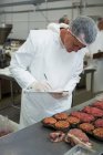 Metzger hält in Fleischfabrik Platten auf Klemmbrett — Stockfoto