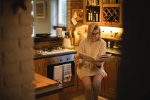 Woman reading a book in kitchen at home — Stock Photo